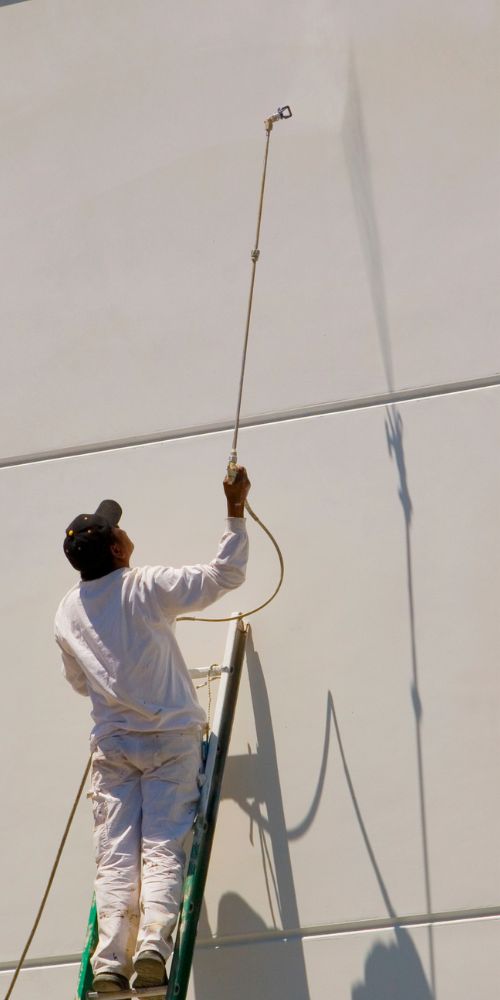 Commercial painting services provider using sprayer on exterior building wall